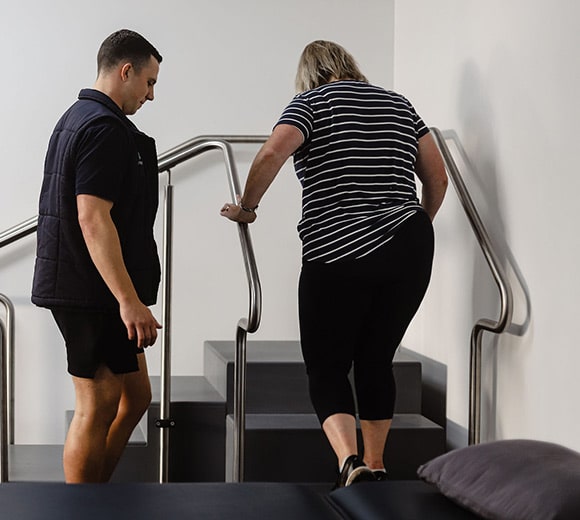 GenHealth - Our Services - General Physiotherapy - Physiotherapist guiding client on stair exercises.
